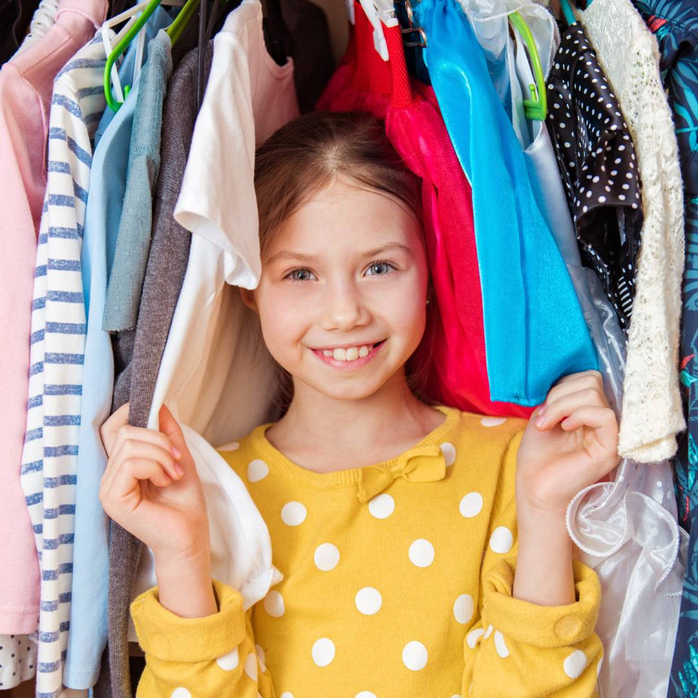 A young girl standing inside of her sustainably-sourced wardrobe, filled with many colorful clothing items.